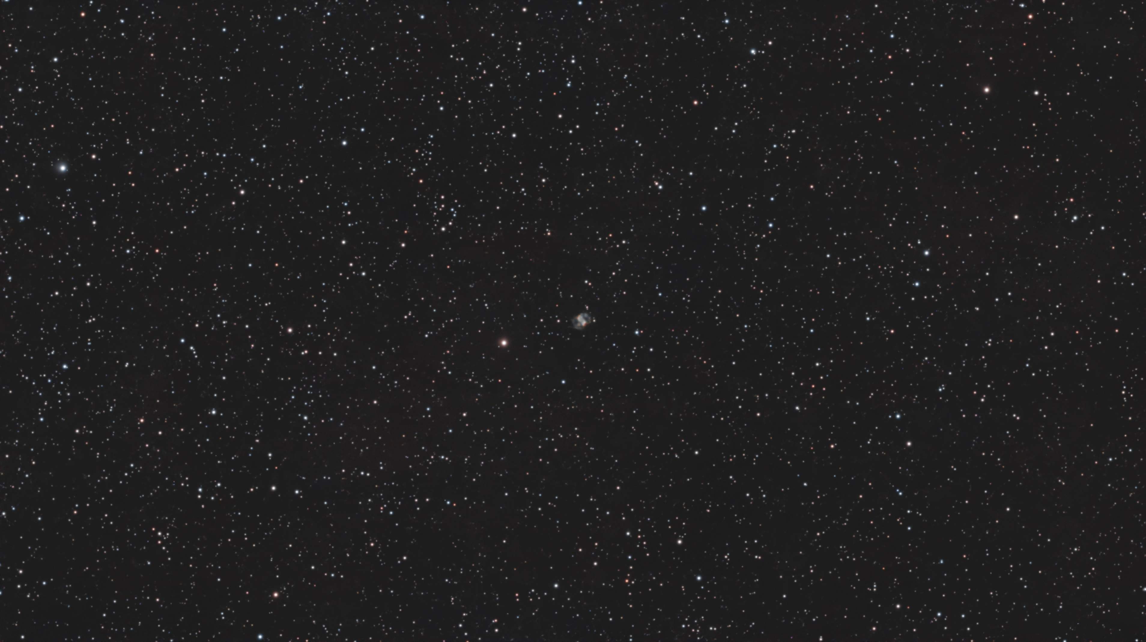 The compact blue-green and reddish lobes of M76 in a dense star field